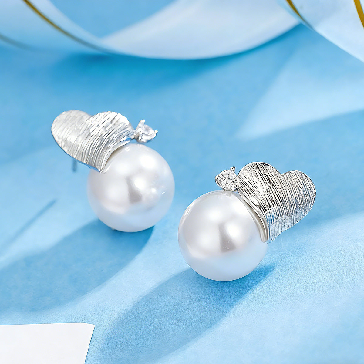 This minimalist pair of silver pearl stud earrings cleverly combine a chic silver heart-shaped pendant (11.7 mm wide) with a striking pearl teardrop (total height: 19.4 mm), with the pearl beneath the heart, creating a unique and stylish silhouette.
