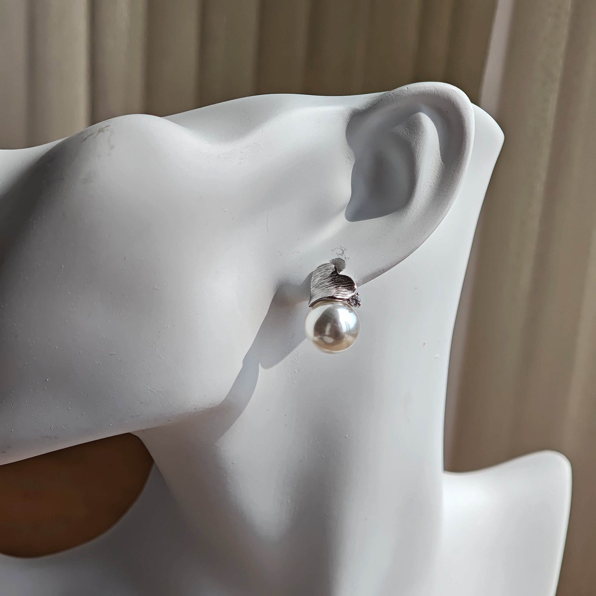 This minimalist pair of silver pearl stud earrings cleverly combine a chic silver heart-shaped pendant (11.7 mm wide) with a striking pearl teardrop (total height: 19.4 mm), with the pearl beneath the heart, creating a unique and stylish silhouette.