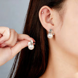 This minimalist pair of silver pearl stud earrings cleverly combine a chic silver heart-shaped pendant (11.7 mm wide) with a striking pearl teardrop (total height: 19.4 mm), with the pearl beneath the heart, creating a unique and stylish silhouette.