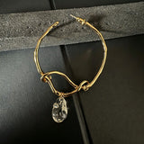 These artistic hoop earrings feature organic, knotted gold-toned metalwork that evokes a natural, twisted vine aesthetic. Suspended from each hoop is a freeform, clear charm with a textured, water-drop shape that catches light beautifully. The contrast between the warm, matte gold and the cool, translucent crystal creates a bold, avant-garde look.