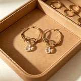 These artistic hoop earrings feature organic, knotted gold-toned metalwork that evokes a natural, twisted vine aesthetic. Suspended from each hoop is a freeform, clear charm with a textured, water-drop shape that catches light beautifully. The contrast between the warm, matte gold and the cool, translucent crystal creates a bold, avant-garde look.