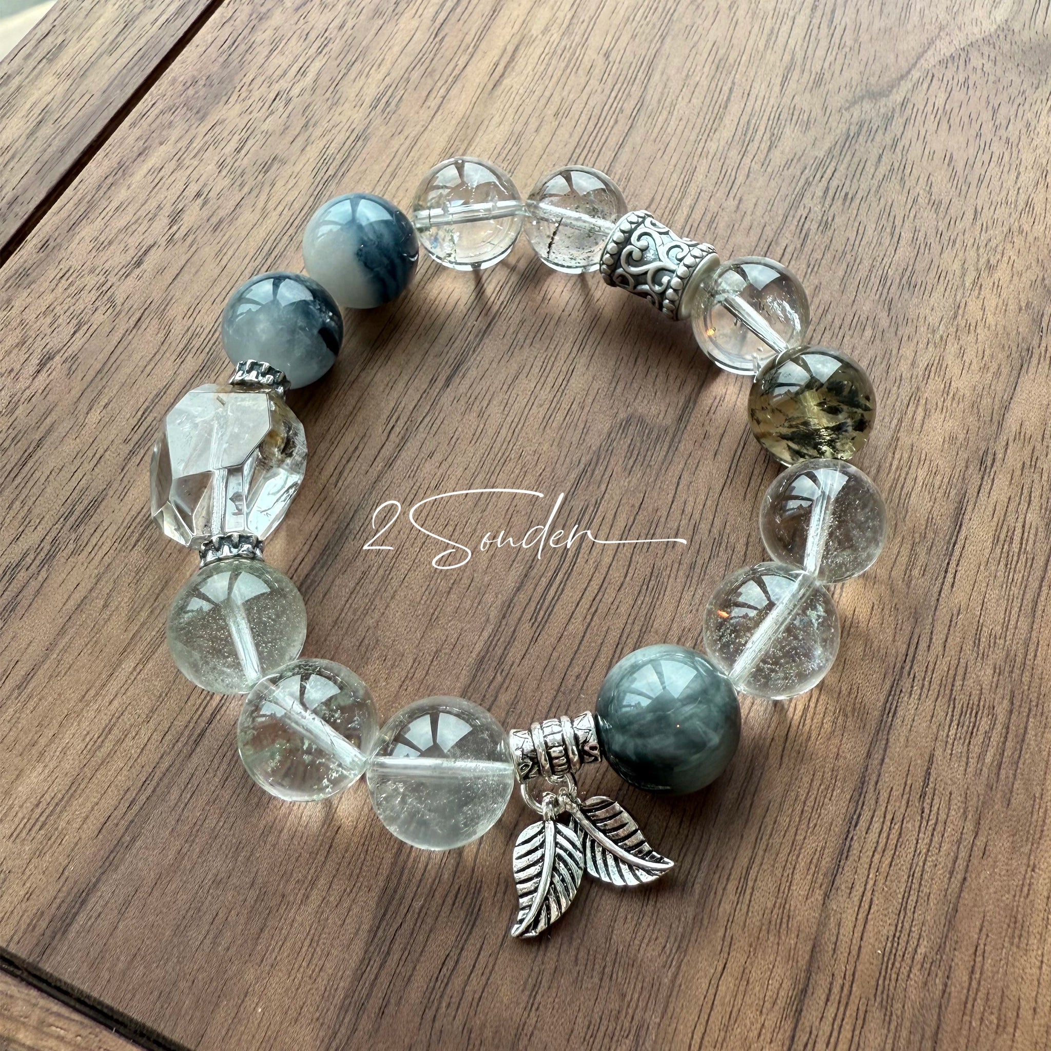 This beaded bracelet is crafted from a mesmerizing combination of Green Phantom Quartz, Blue Rabbit Hair Quartz, Hawk's Eye, Black Aurora Super Seven, and Herkimer. All the beads are natural crystals. The natural patterns of the crystals intertwine beautifully with the metallic accents, creating a unique and enchanting piece.