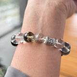 This beaded bracelet is crafted from a mesmerizing combination of Green Phantom Quartz, Blue Rabbit Hair Quartz, Hawk's Eye, Black Aurora Super Seven, and Herkimer. All the beads are natural crystals. The natural patterns of the crystals intertwine beautifully with the metallic accents, creating a unique and enchanting piece.