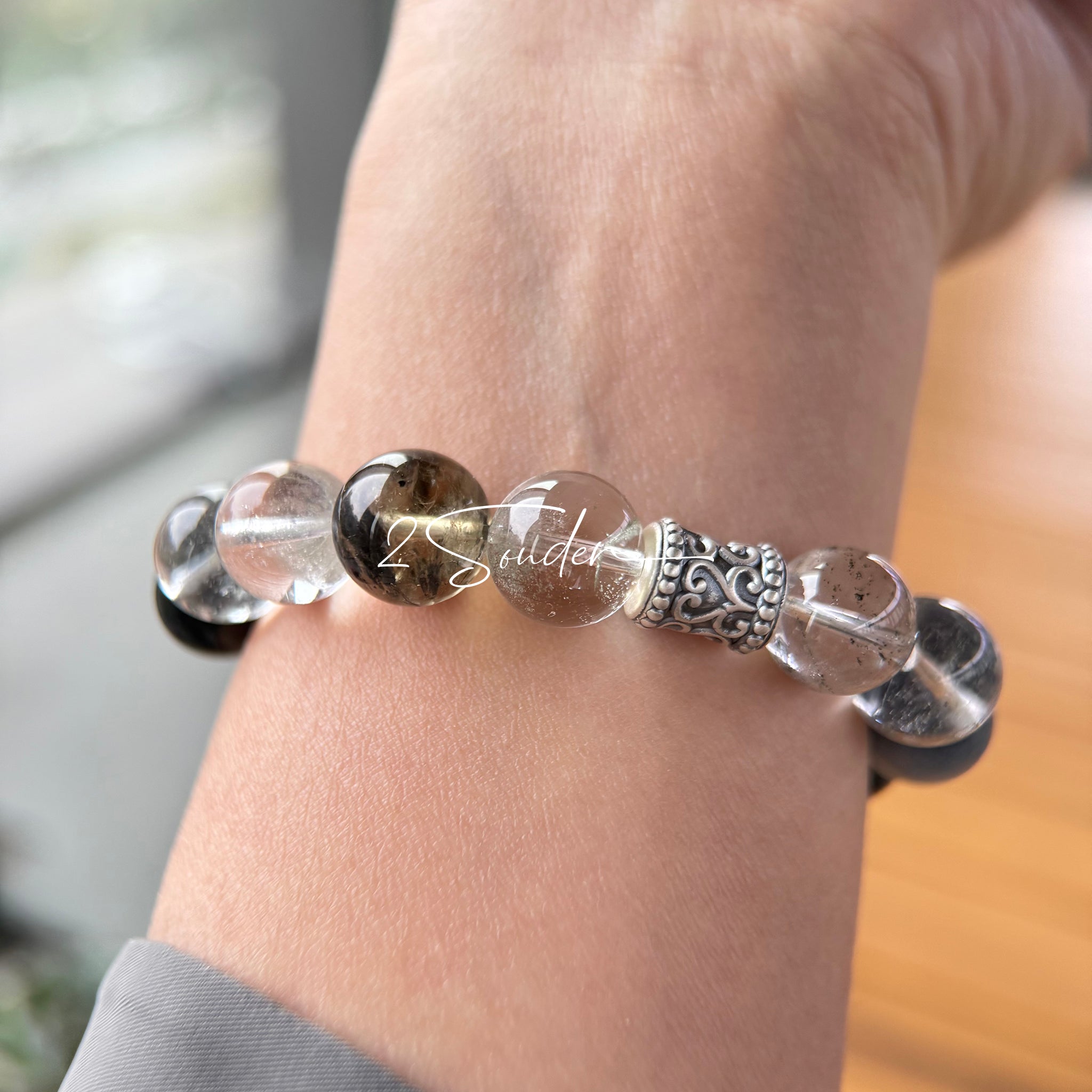 This beaded bracelet is crafted from a mesmerizing combination of Green Phantom Quartz, Blue Rabbit Hair Quartz, Hawk's Eye, Black Aurora Super Seven, and Herkimer. All the beads are natural crystals. The natural patterns of the crystals intertwine beautifully with the metallic accents, creating a unique and enchanting piece.