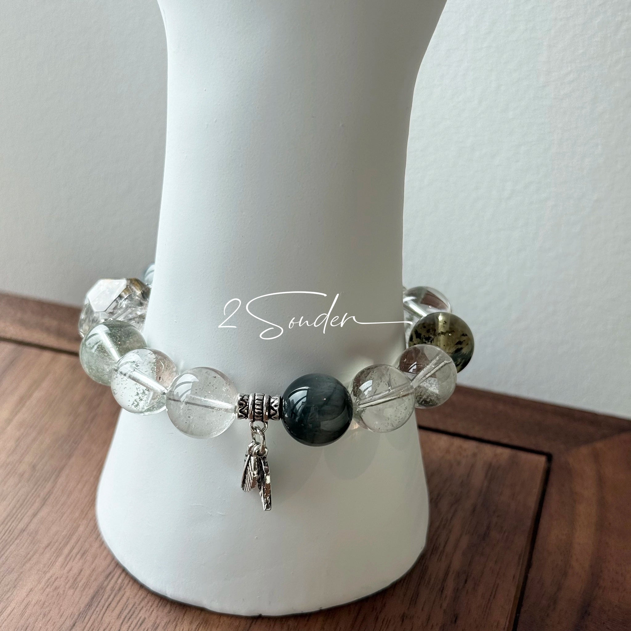 This beaded bracelet is crafted from a mesmerizing combination of Green Phantom Quartz, Blue Rabbit Hair Quartz, Hawk's Eye, Black Aurora Super Seven, and Herkimer. All the beads are natural crystals. The natural patterns of the crystals intertwine beautifully with the metallic accents, creating a unique and enchanting piece.