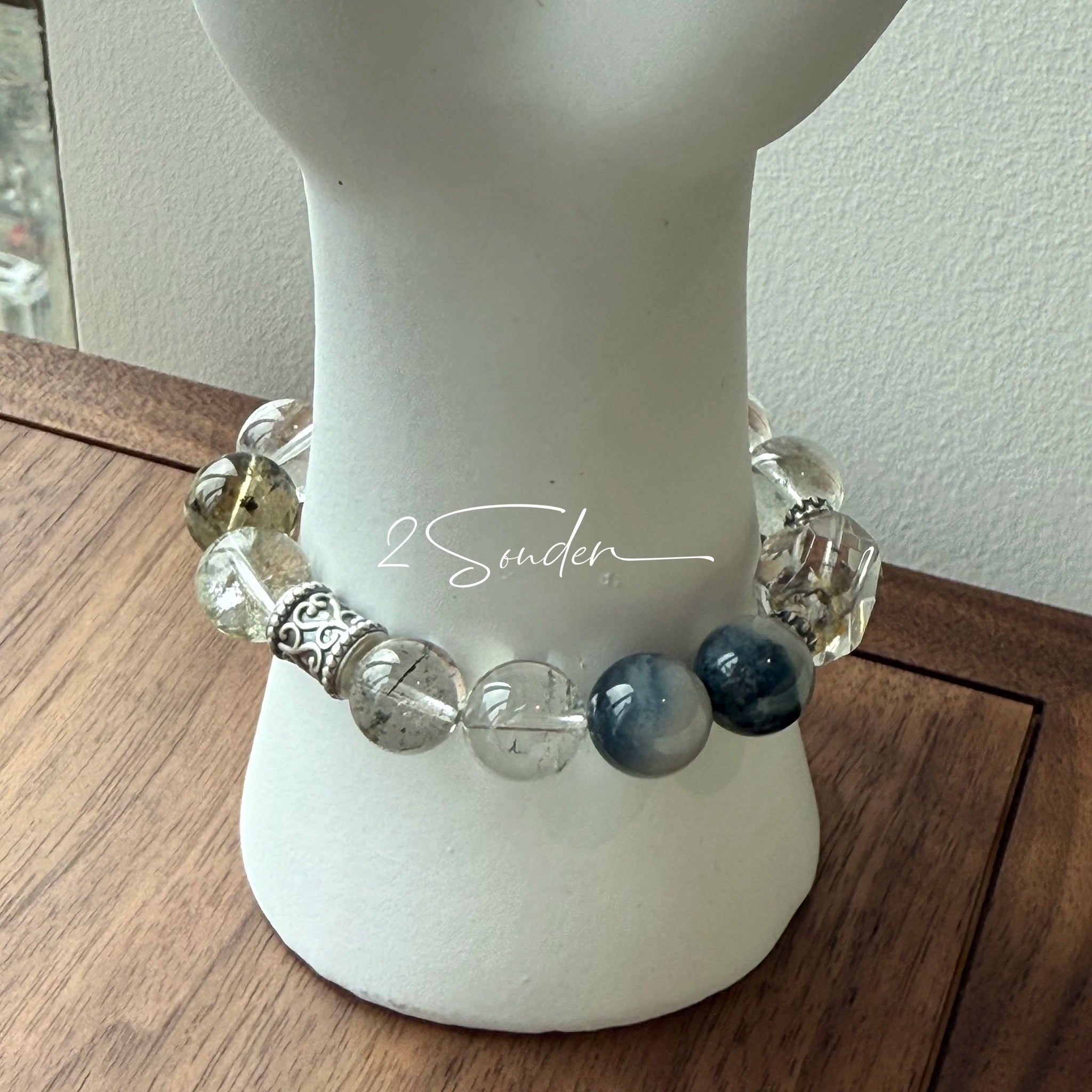This beaded bracelet is crafted from a mesmerizing combination of Green Phantom Quartz, Blue Rabbit Hair Quartz, Hawk's Eye, Black Aurora Super Seven, and Herkimer. All the beads are natural crystals. The natural patterns of the crystals intertwine beautifully with the metallic accents, creating a unique and enchanting piece.