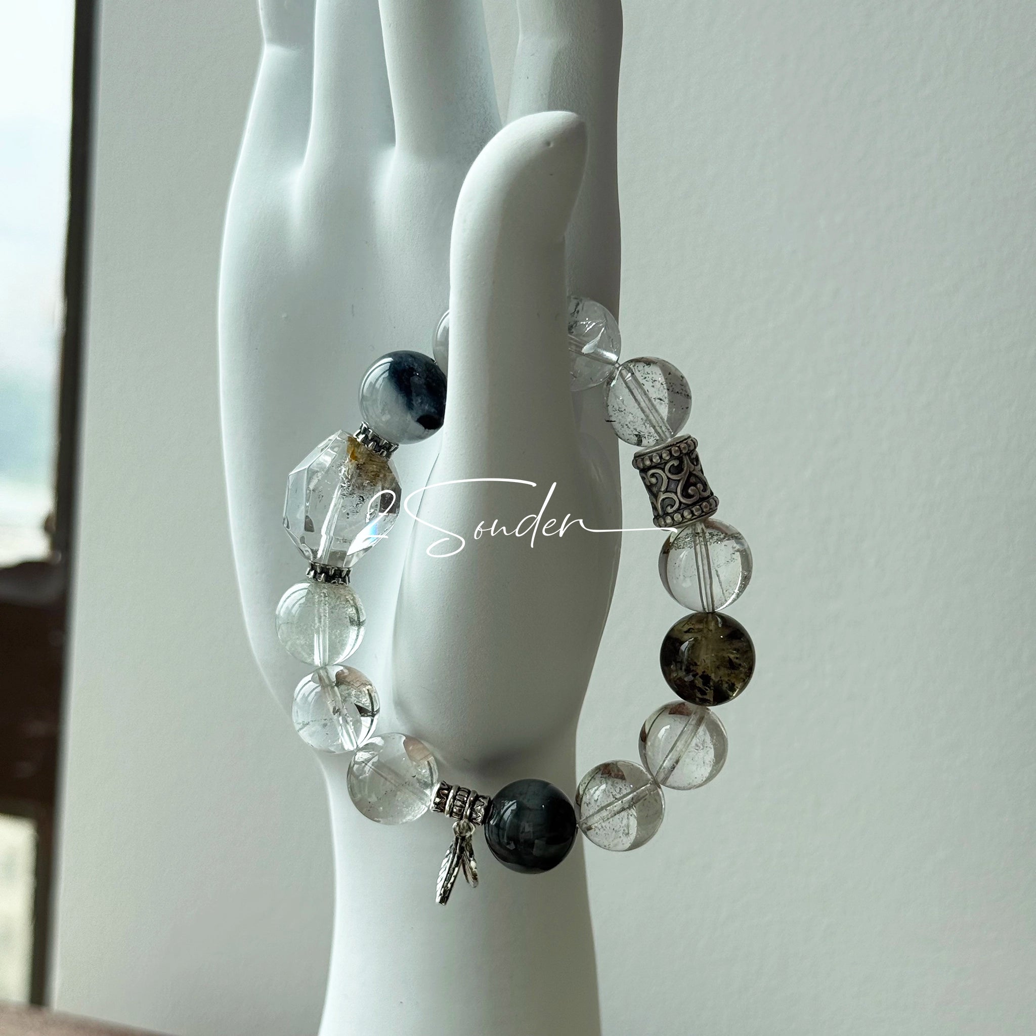 This beaded bracelet is crafted from a mesmerizing combination of Green Phantom Quartz, Blue Rabbit Hair Quartz, Hawk's Eye, Black Aurora Super Seven, and Herkimer. All the beads are natural crystals. The natural patterns of the crystals intertwine beautifully with the metallic accents, creating a unique and enchanting piece.