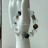This beaded bracelet is crafted from a mesmerizing combination of Green Phantom Quartz, Blue Rabbit Hair Quartz, Hawk's Eye, Black Aurora Super Seven, and Herkimer. All the beads are natural crystals. The natural patterns of the crystals intertwine beautifully with the metallic accents, creating a unique and enchanting piece.