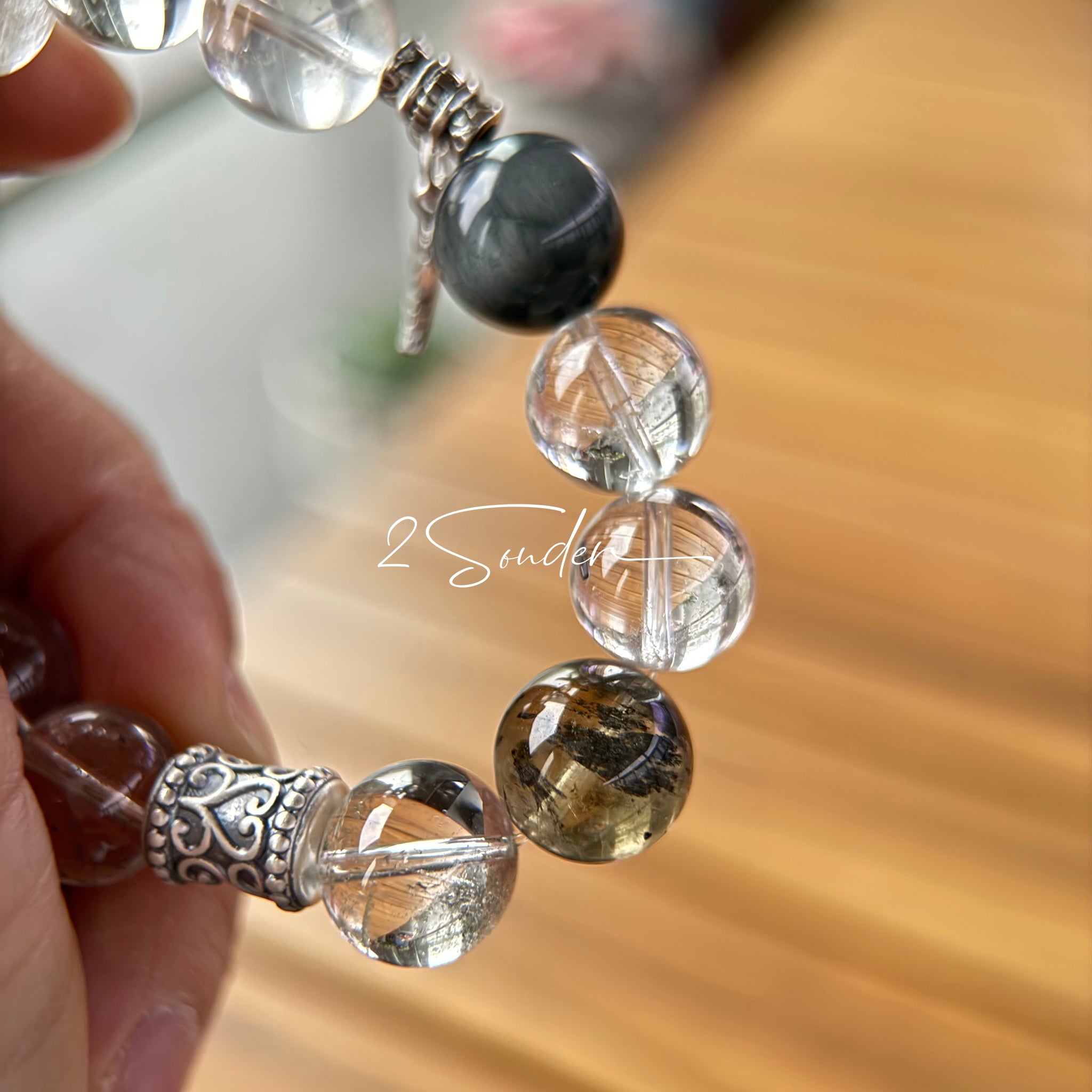 This beaded bracelet is crafted from a mesmerizing combination of Green Phantom Quartz, Blue Rabbit Hair Quartz, Hawk's Eye, Black Aurora Super Seven, and Herkimer. All the beads are natural crystals. The natural patterns of the crystals intertwine beautifully with the metallic accents, creating a unique and enchanting piece.