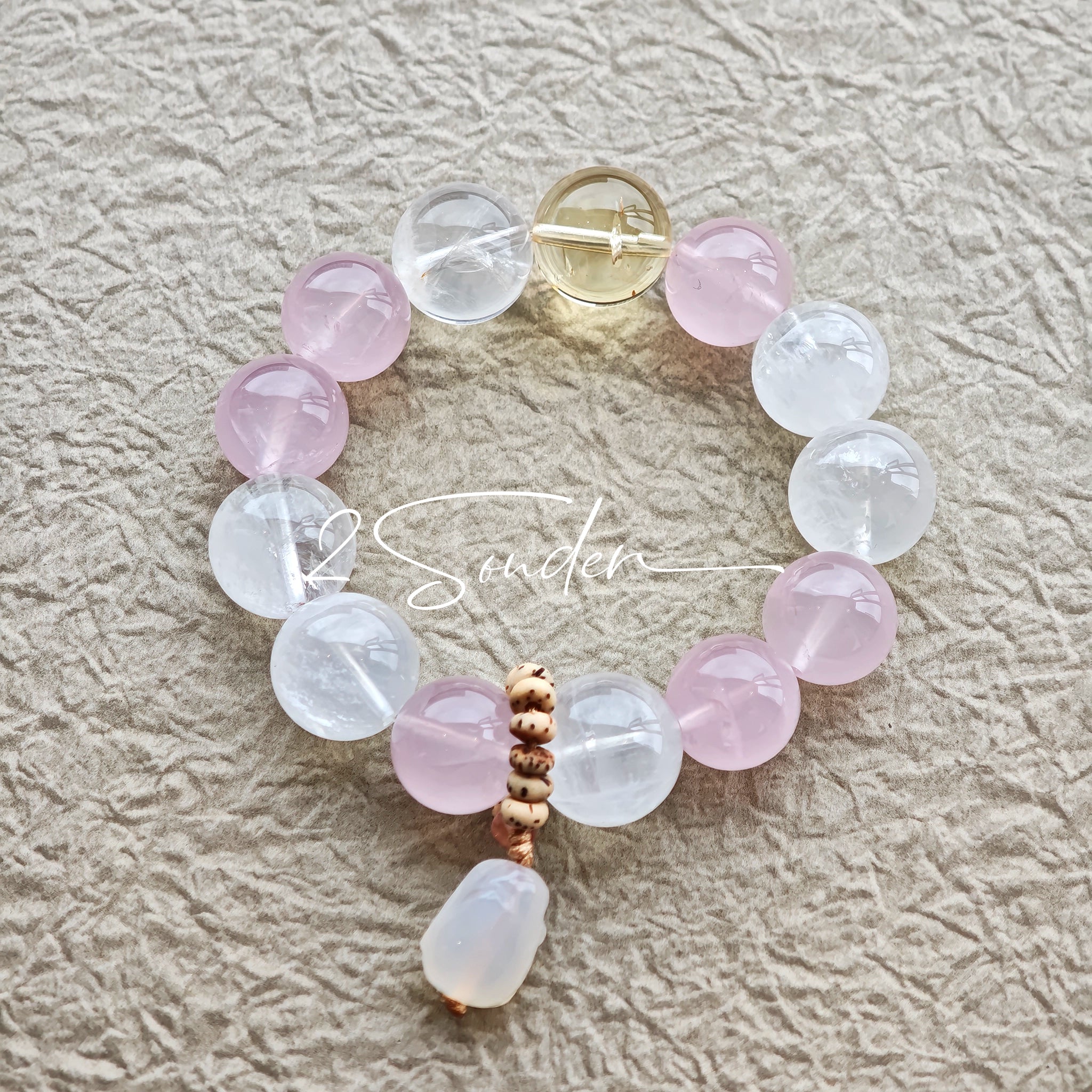 This natural crystal bracelet features a serene mix of white phantom quartz, soft rose quartz, and luminous citrine beads, creating a light, airy aesthetic. Adorned with delicate star-and-moon bodhi seed accents and a milky white chalcedony pendant, it adds a touch of gentle elegance to everyday wear.