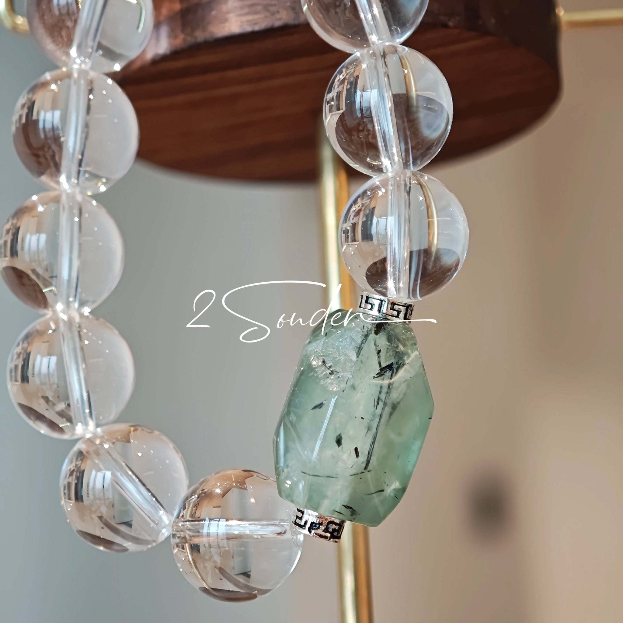 This stunning bracelet is crafted with a strand of perfectly round, high-clarity clear quartz beads, showcasing exceptional transparency and a brilliant, glass-like luster. At its center sits a striking free-form green gemstone accent, its natural inclusions and unique cut adding a one-of-a-kind, organic touch. The two stones are elegantly separated by delicate silver-toned decorative spacers, creating a balanced, sophisticated design that blends minimalist clarity with bold natural beauty.