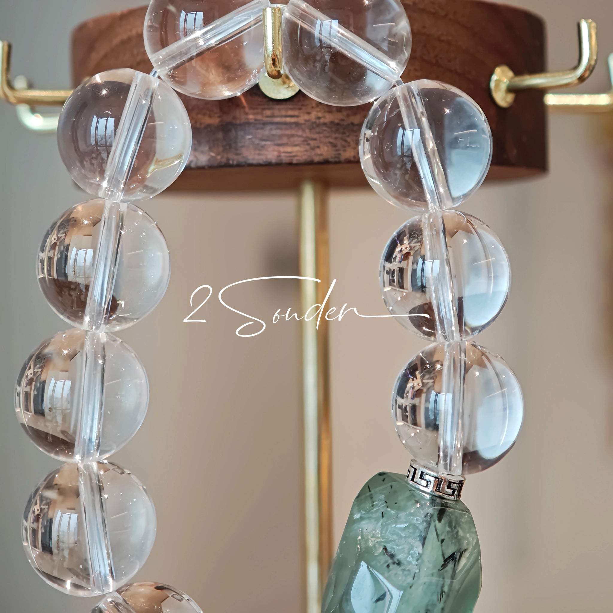 This stunning bracelet is crafted with a strand of perfectly round, high-clarity clear quartz beads, showcasing exceptional transparency and a brilliant, glass-like luster. At its center sits a striking free-form green gemstone accent, its natural inclusions and unique cut adding a one-of-a-kind, organic touch. The two stones are elegantly separated by delicate silver-toned decorative spacers, creating a balanced, sophisticated design that blends minimalist clarity with bold natural beauty.