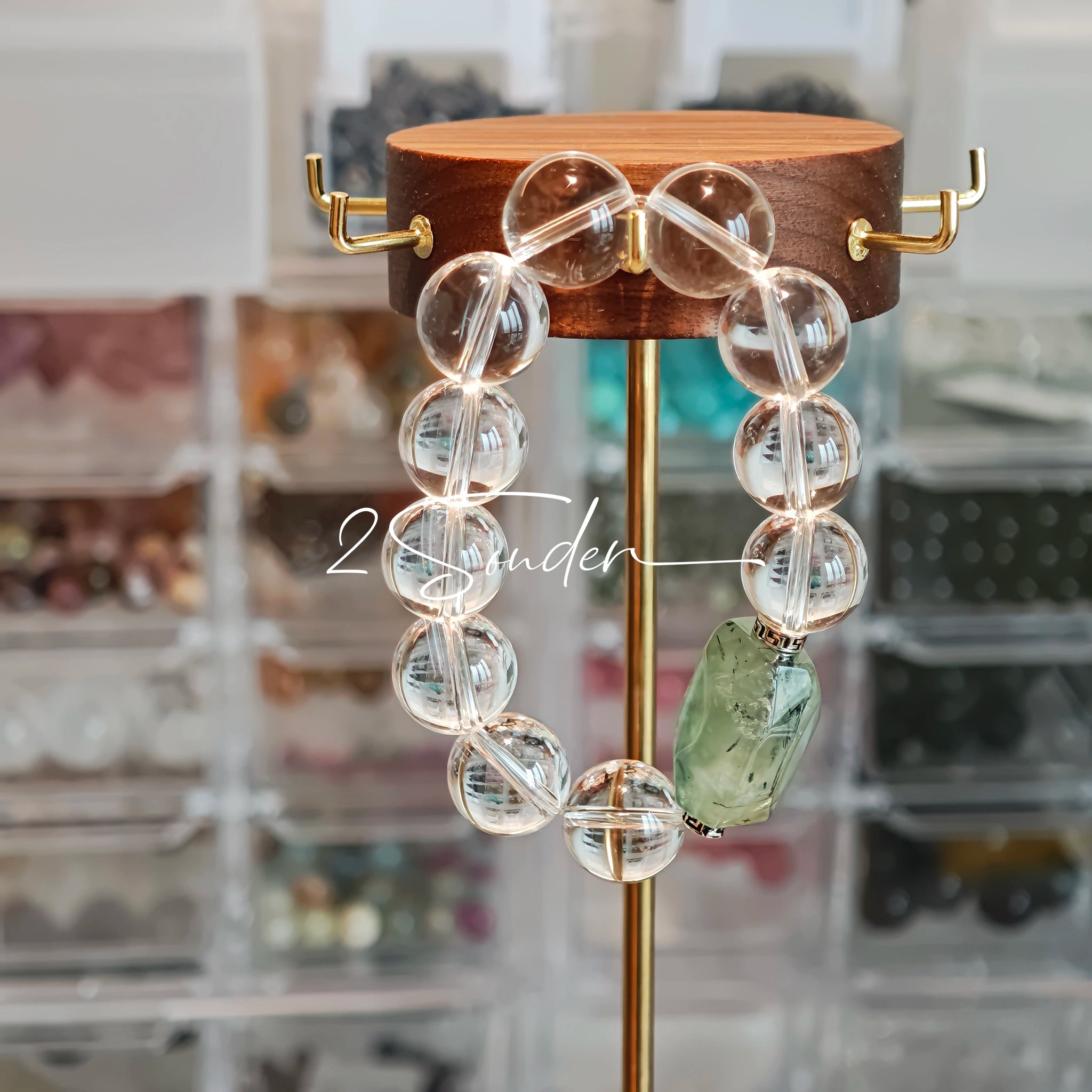 This stunning bracelet is crafted with a strand of perfectly round, high-clarity clear quartz beads, showcasing exceptional transparency and a brilliant, glass-like luster. At its center sits a striking free-form green gemstone accent, its natural inclusions and unique cut adding a one-of-a-kind, organic touch. The two stones are elegantly separated by delicate silver-toned decorative spacers, creating a balanced, sophisticated design that blends minimalist clarity with bold natural beauty.