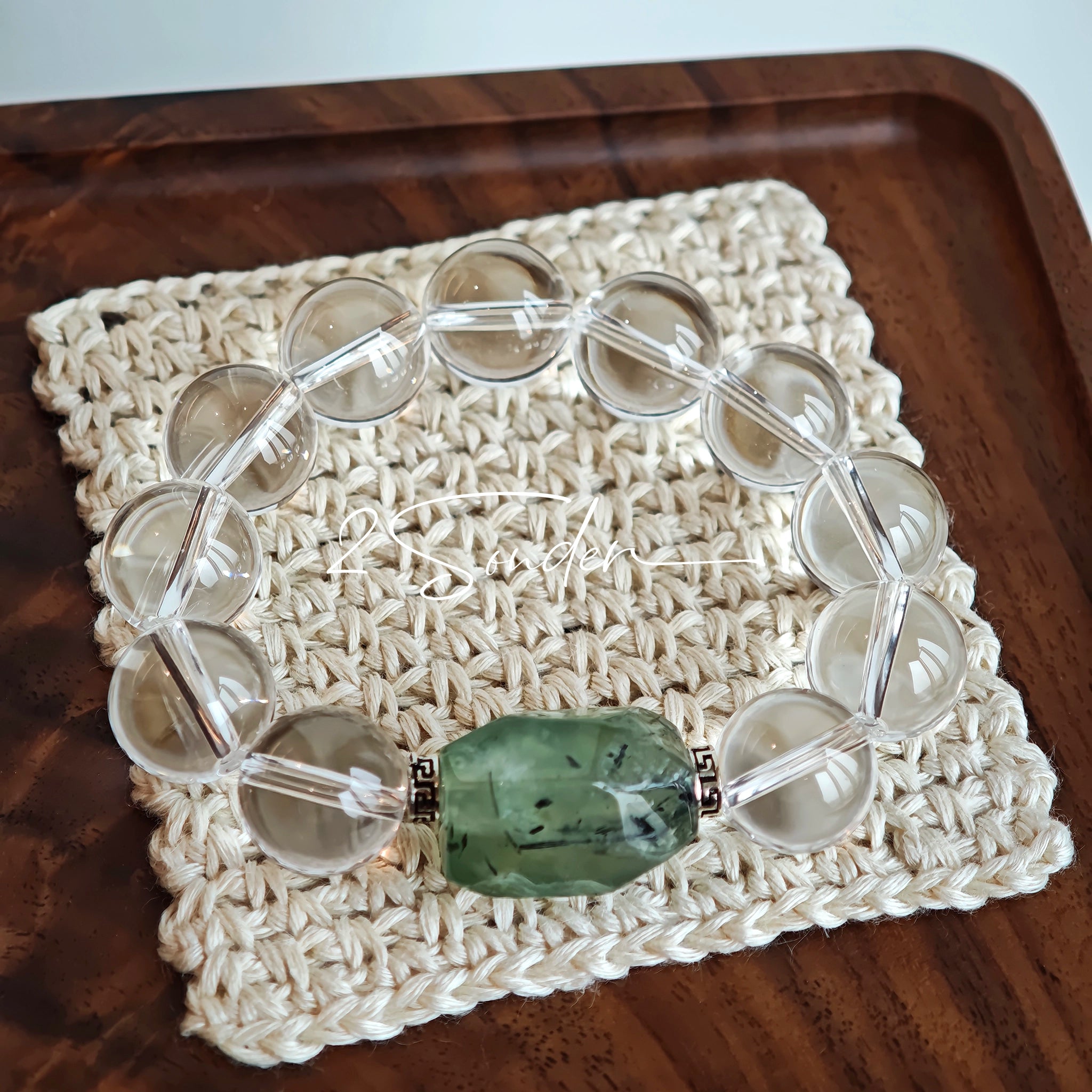 This stunning bracelet is crafted with a strand of perfectly round, high-clarity clear quartz beads, showcasing exceptional transparency and a brilliant, glass-like luster. At its center sits a striking free-form green gemstone accent, its natural inclusions and unique cut adding a one-of-a-kind, organic touch. The two stones are elegantly separated by delicate silver-toned decorative spacers, creating a balanced, sophisticated design that blends minimalist clarity with bold natural beauty.