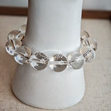 This stunning bracelet is crafted with a strand of perfectly round, high-clarity clear quartz beads, showcasing exceptional transparency and a brilliant, glass-like luster. At its center sits a striking free-form green gemstone accent, its natural inclusions and unique cut adding a one-of-a-kind, organic touch. The two stones are elegantly separated by delicate silver-toned decorative spacers, creating a balanced, sophisticated design that blends minimalist clarity with bold natural beauty.