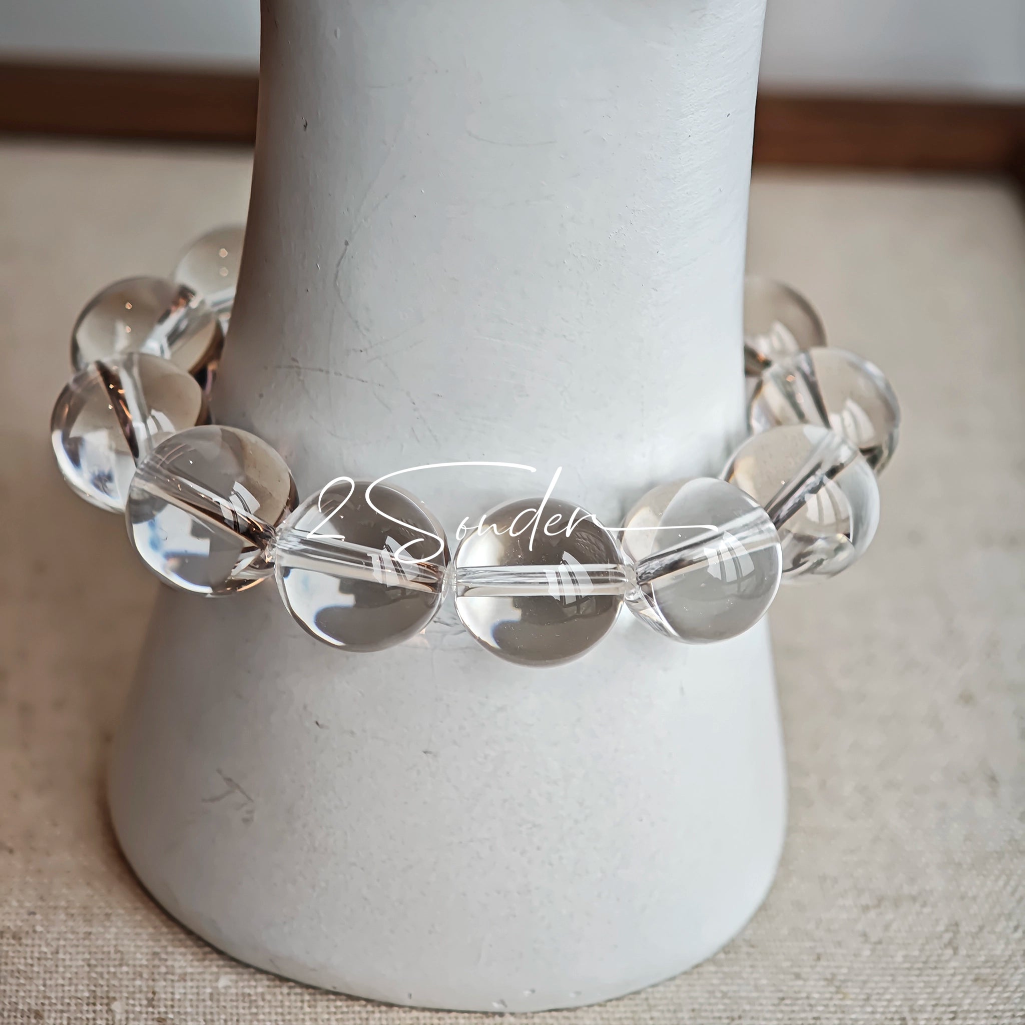 This stunning bracelet is crafted with a strand of perfectly round, high-clarity clear quartz beads, showcasing exceptional transparency and a brilliant, glass-like luster. At its center sits a striking free-form green gemstone accent, its natural inclusions and unique cut adding a one-of-a-kind, organic touch. The two stones are elegantly separated by delicate silver-toned decorative spacers, creating a balanced, sophisticated design that blends minimalist clarity with bold natural beauty.