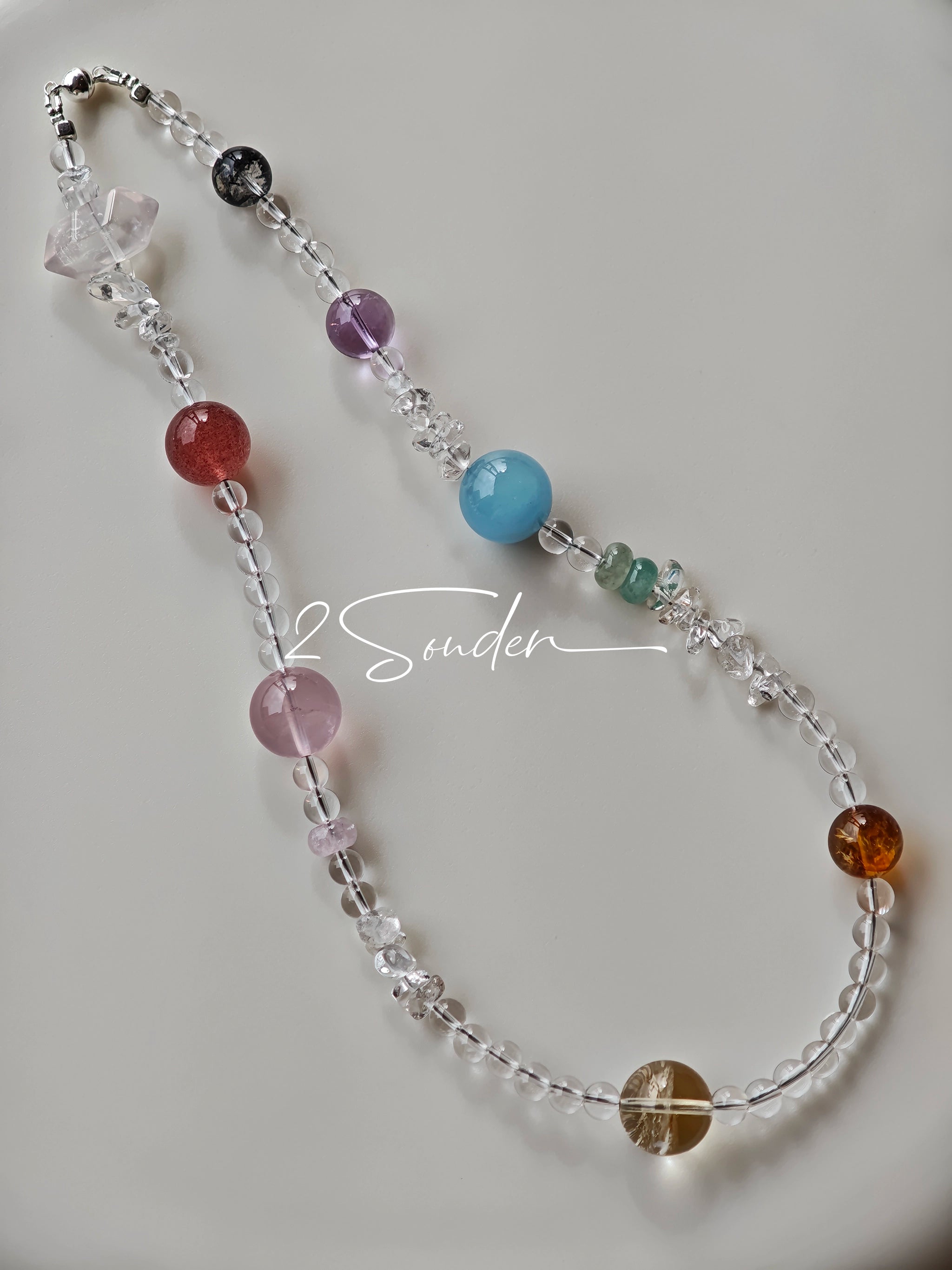 This handcrafted gemstone necklace is a stunning blend of natural crystals, featuring sparkling Herkimer Diamonds, vibrant Brazilian Amethyst, rich Pigeon's Blood Strawberry Quartz, serene Aquamarine, sunny Citrine, and luminous clear quartz, each bead hand-selected for its one-of-a-kind beauty. Strung alongside polished clear quartz spacers and accent stones, the necklace balances bold, colorful statement beads with delicate, shimmering crystal details, creating a piece that feels both earthy and ethereal.