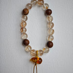 The bracelet braids lightning (copper rutile) with incense (agarwood) and ties the knot under a flowery lucky gourd.