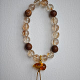 The bracelet braids lightning (copper rutile) with incense (agarwood) and ties the knot under a flowery lucky gourd.