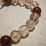 The bracelet pairs power crystals and sacred wood, then lets a flower-amber calabash dangle its twin seeds: prosper, protect.