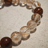 The bracelet pairs power crystals and sacred wood, then lets a flower-amber calabash dangle its twin seeds: prosper, protect.