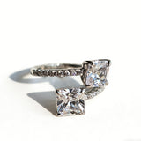 This striking bypass ring showcases two large, brilliant cushion-cut clear stones held securely in classic four-prong settings. The elegant twisted band is lined with a row of sparkling accent Cubic Zirconia stones, delivering a high-end, light luxury aesthetic that instantly catches the eye.