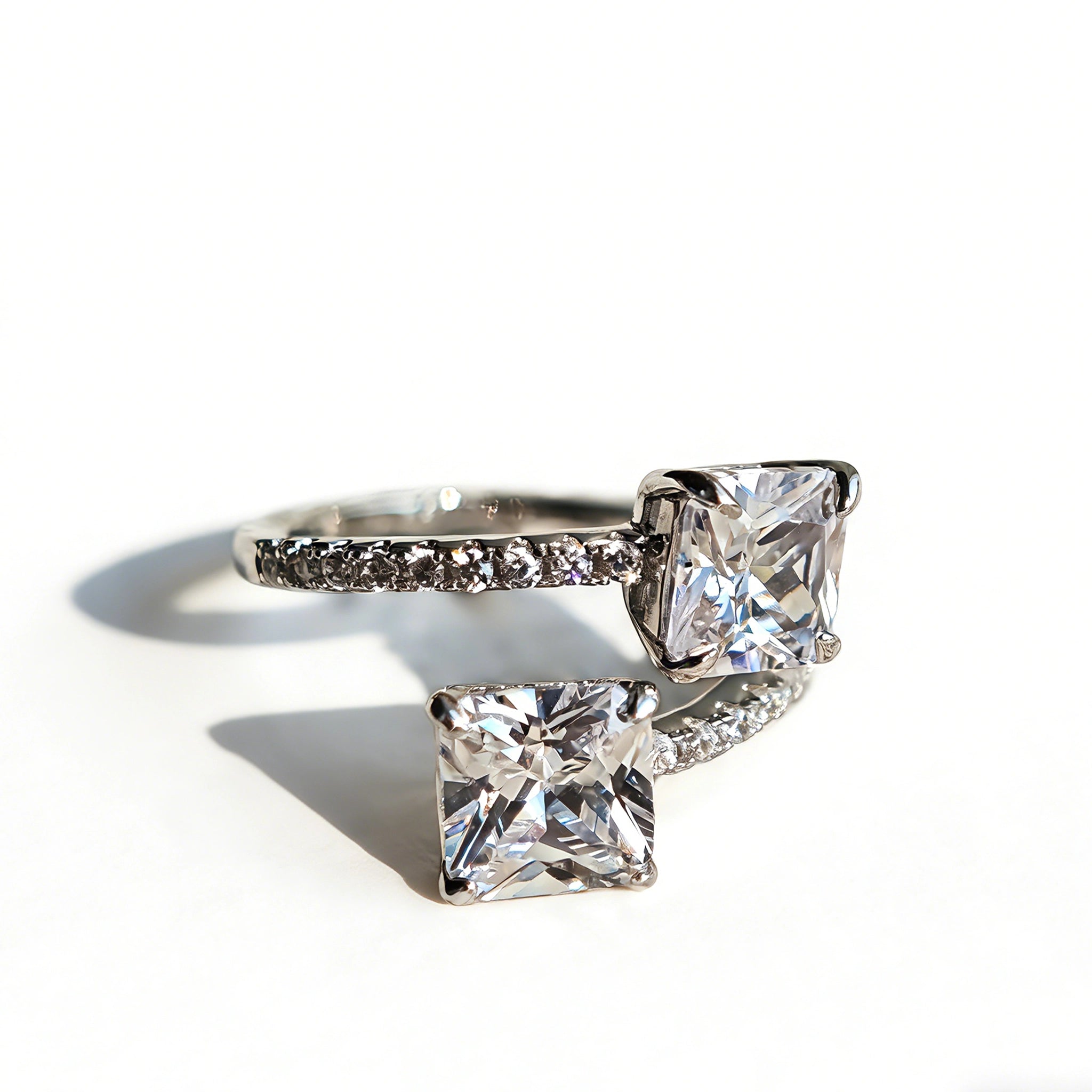 This striking bypass ring showcases two large, brilliant cushion-cut clear stones held securely in classic four-prong settings. The elegant twisted band is lined with a row of sparkling accent Cubic Zirconia stones, delivering a high-end, light luxury aesthetic that instantly catches the eye.