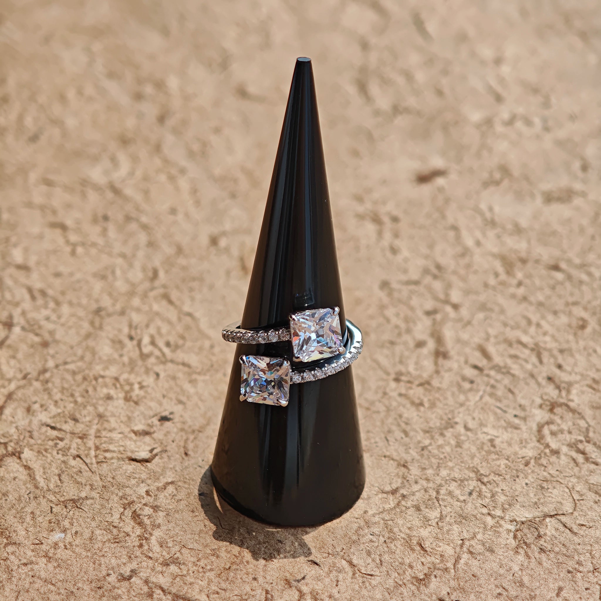 This striking bypass ring showcases two large, brilliant cushion-cut clear stones held securely in classic four-prong settings. The elegant twisted band is lined with a row of sparkling accent Cubic Zirconia stones, delivering a high-end, light luxury aesthetic that instantly catches the eye.