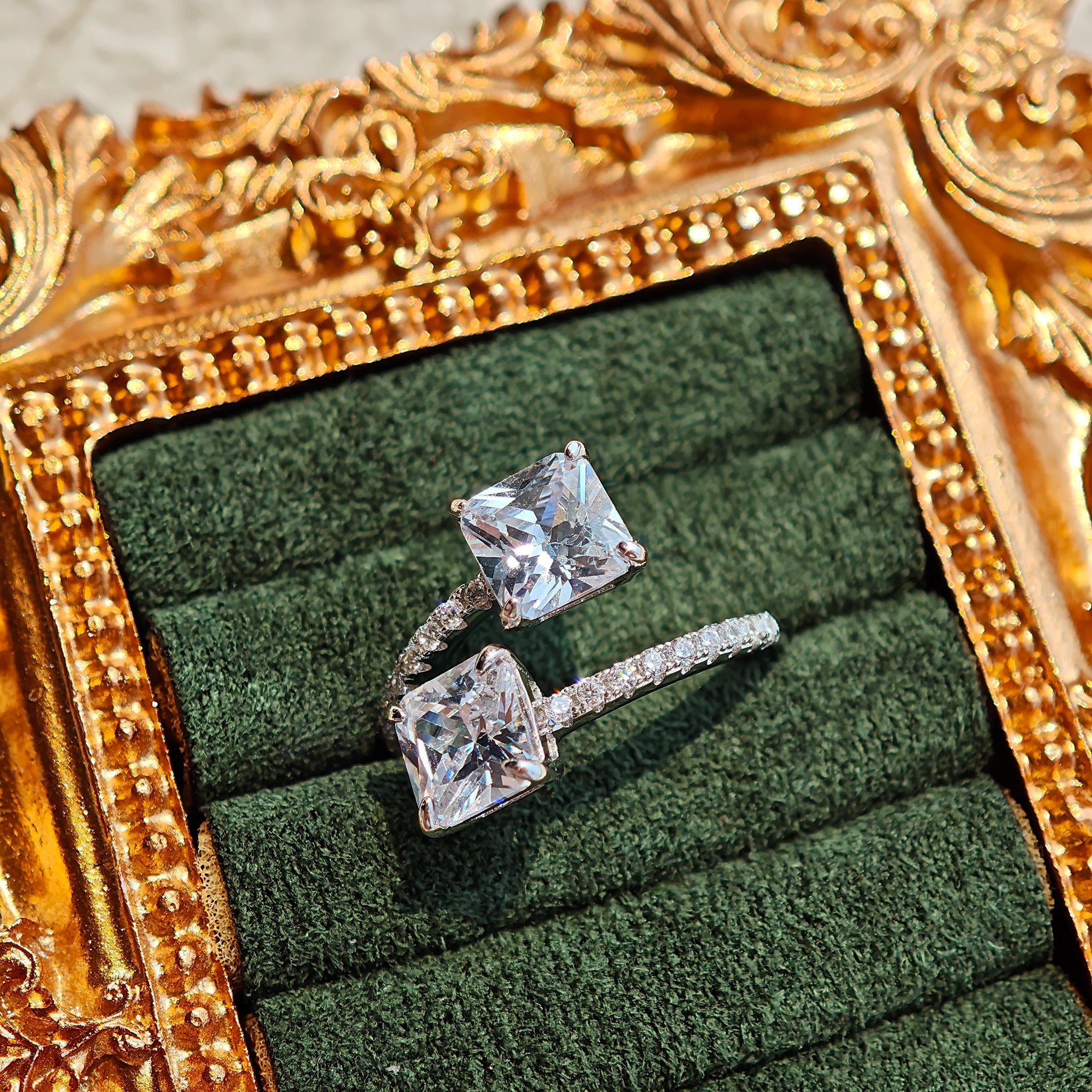 This striking bypass ring showcases two large, brilliant cushion-cut clear stones held securely in classic four-prong settings. The elegant twisted band is lined with a row of sparkling accent Cubic Zirconia stones, delivering a high-end, light luxury aesthetic that instantly catches the eye.