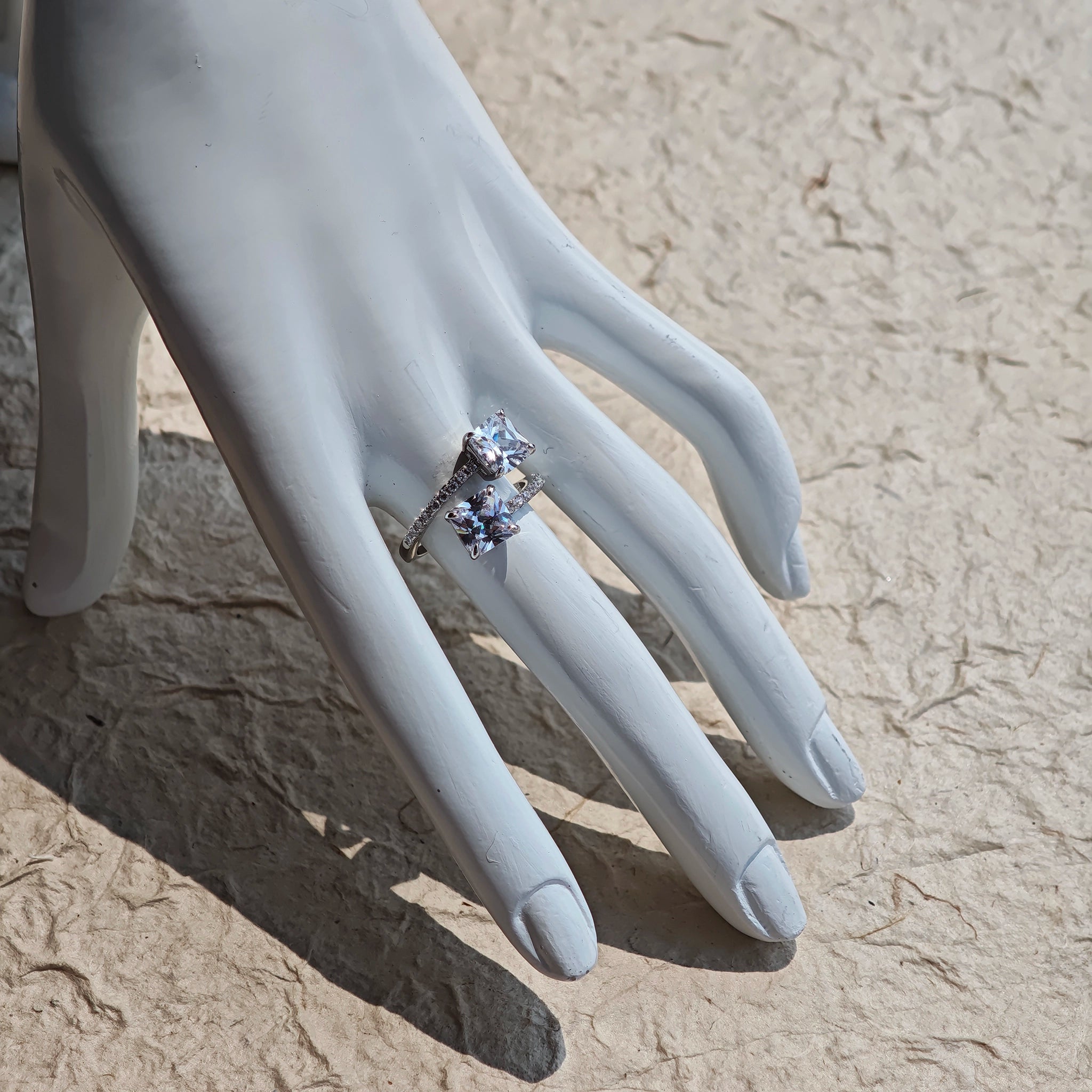 This striking bypass ring showcases two large, brilliant cushion-cut clear stones held securely in classic four-prong settings. The elegant twisted band is lined with a row of sparkling accent Cubic Zirconia stones, delivering a high-end, light luxury aesthetic that instantly catches the eye.