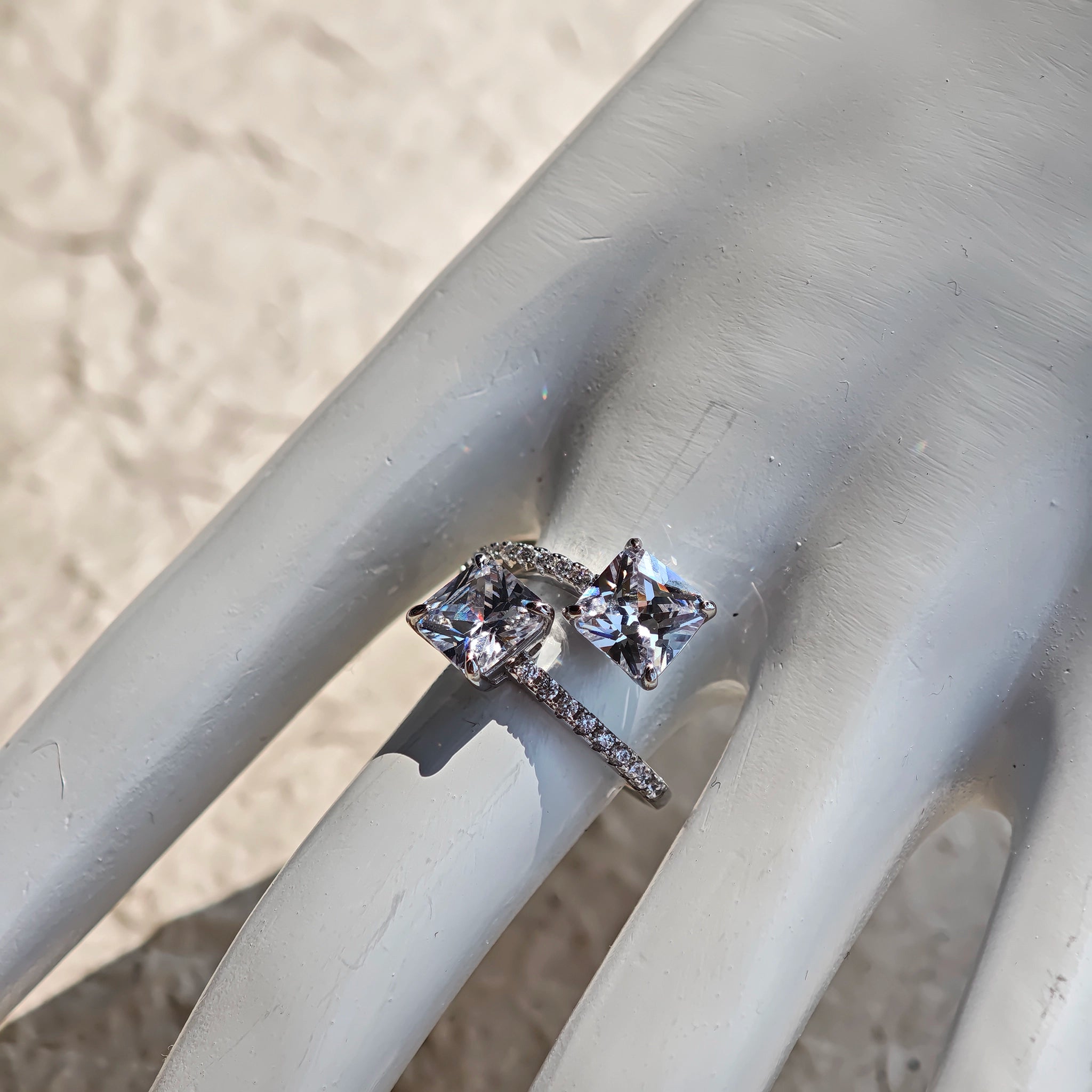 This striking bypass ring showcases two large, brilliant cushion-cut clear stones held securely in classic four-prong settings. The elegant twisted band is lined with a row of sparkling accent Cubic Zirconia stones, delivering a high-end, light luxury aesthetic that instantly catches the eye.