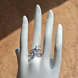 This striking bypass ring showcases two large, brilliant cushion-cut clear stones held securely in classic four-prong settings. The elegant twisted band is lined with a row of sparkling accent Cubic Zirconia stones, delivering a high-end, light luxury aesthetic that instantly catches the eye.