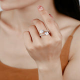 This striking bypass ring showcases two large, brilliant cushion-cut clear stones held securely in classic four-prong settings. The elegant twisted band is lined with a row of sparkling accent Cubic Zirconia stones, delivering a high-end, light luxury aesthetic that instantly catches the eye.
