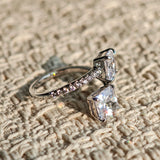 This striking bypass ring showcases two large, brilliant cushion-cut clear stones held securely in classic four-prong settings. The elegant twisted band is lined with a row of sparkling accent Cubic Zirconia stones, delivering a high-end, light luxury aesthetic that instantly catches the eye.