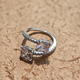 This striking bypass ring showcases two large, brilliant cushion-cut clear stones held securely in classic four-prong settings. The elegant twisted band is lined with a row of sparkling accent Cubic Zirconia stones, delivering a high-end, light luxury aesthetic that instantly catches the eye.
