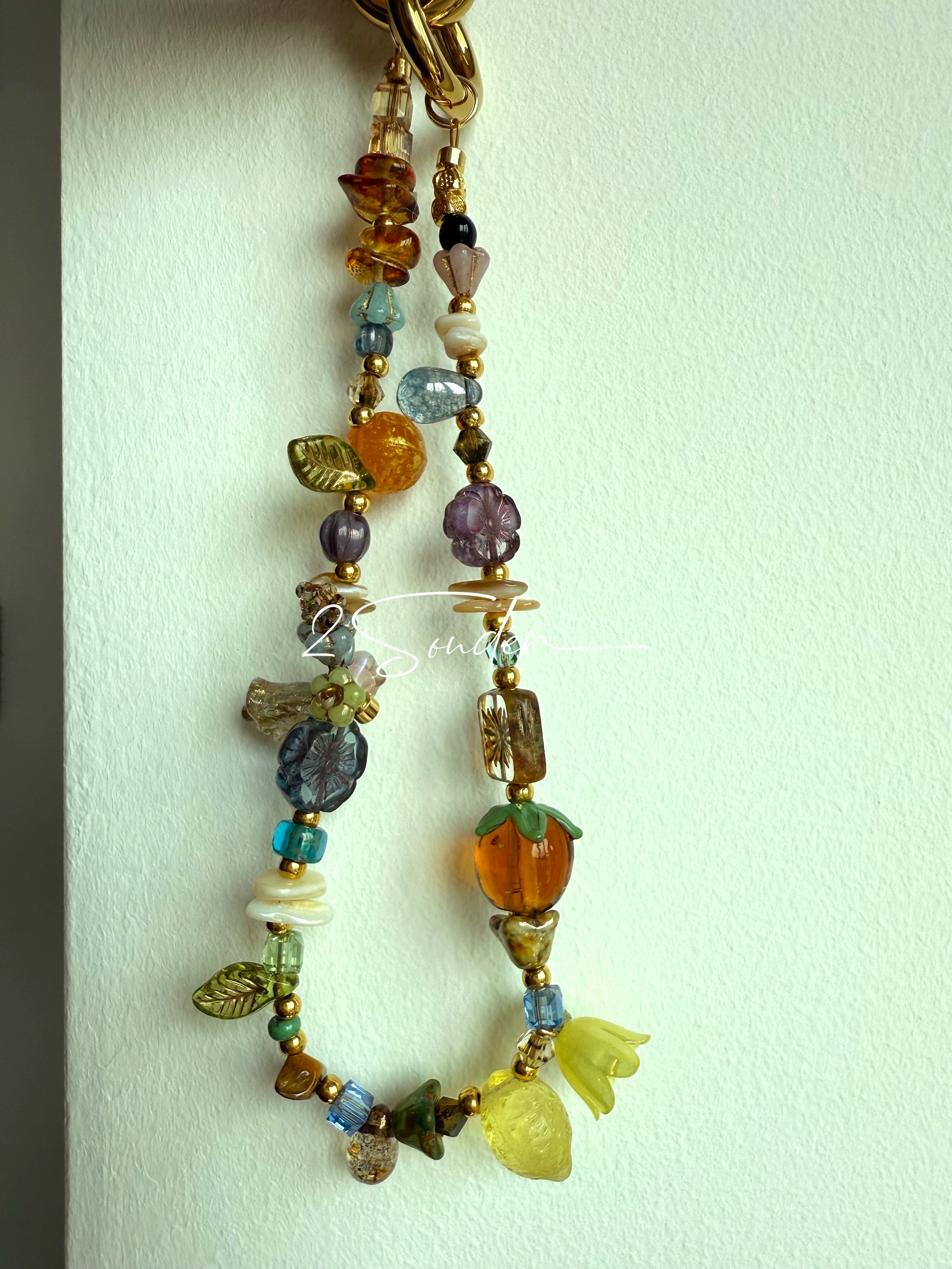 This is a bag charm that made of Czech beads. In the phone strap, there are different spacers like orange, leaves, flowers and lemon. It's with multi colors. This bag charm can also be used as a phone strap and key chain.