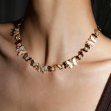 This delicate choker necklace features alternating polished metal butterflies and lustrous white mother-of-pearl butterflies, accented with tiny sparkling crystals. The shimmering white shell inlays contrast beautifully with the warm gold (or cool silver) metal finish, creating an elegant, whimsical design that sits close to the collarbone.