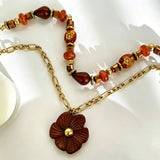 This vintage‑inspired Meidelat layered necklace features warm amber‑toned beads paired with polished gold‑toned metal chains. A carved rich brown flower pendant hangs on the lower paperclip chain, while the upper strand mixes varied-shaped resin beads for textured depth. Perfect for creating cozy boho‑chic layered neck stacking looks.