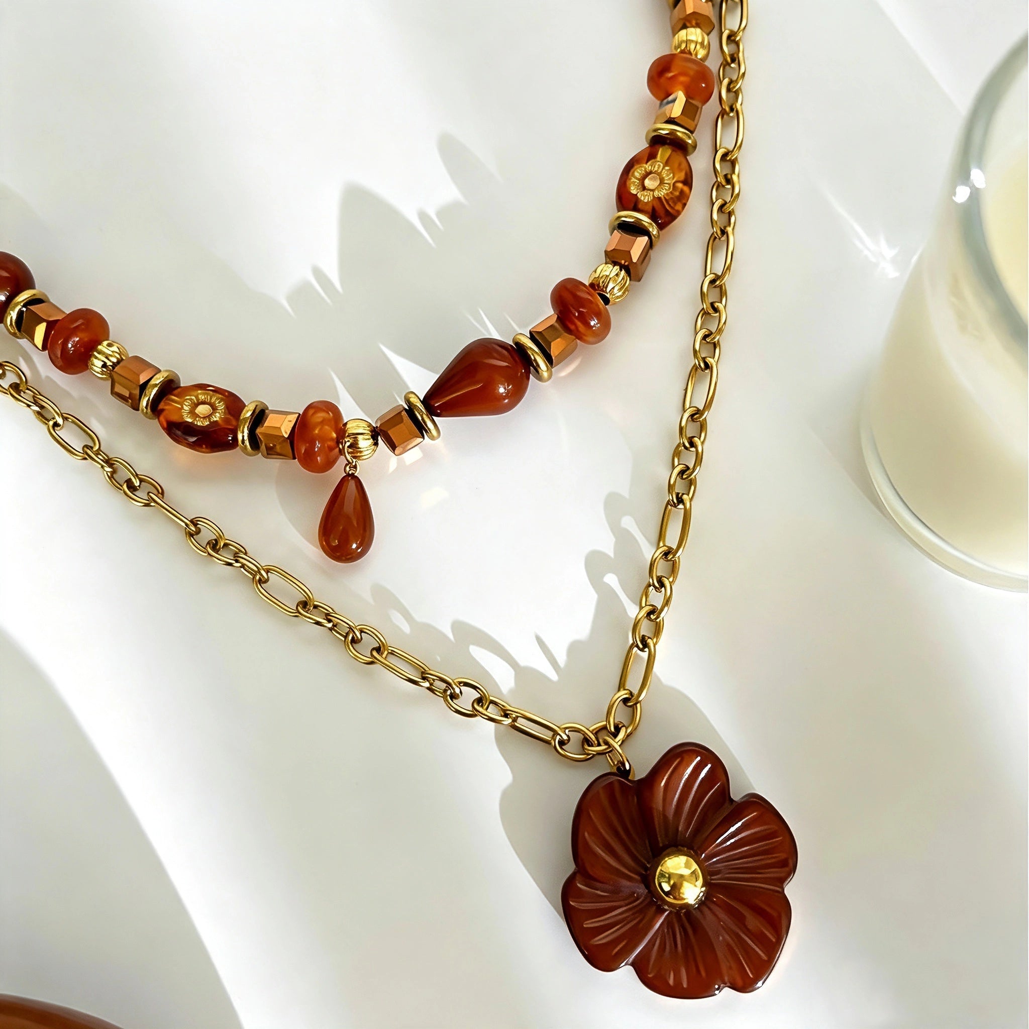 This vintage‑inspired Meidelat layered necklace features warm amber‑toned beads paired with polished gold‑toned metal chains. A carved rich brown flower pendant hangs on the lower paperclip chain, while the upper strand mixes varied-shaped resin beads for textured depth. Perfect for creating cozy boho‑chic layered neck stacking looks.