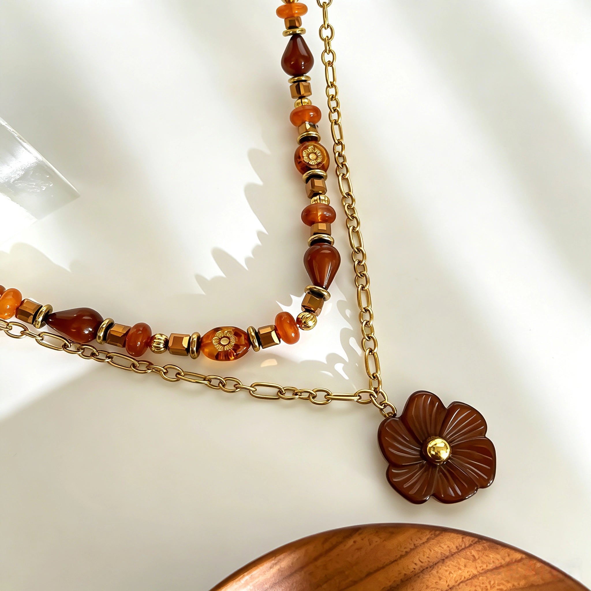 This vintage‑inspired Meidelat layered necklace features warm amber‑toned beads paired with polished gold‑toned metal chains. A carved rich brown flower pendant hangs on the lower paperclip chain, while the upper strand mixes varied-shaped resin beads for textured depth. Perfect for creating cozy boho‑chic layered neck stacking looks.
