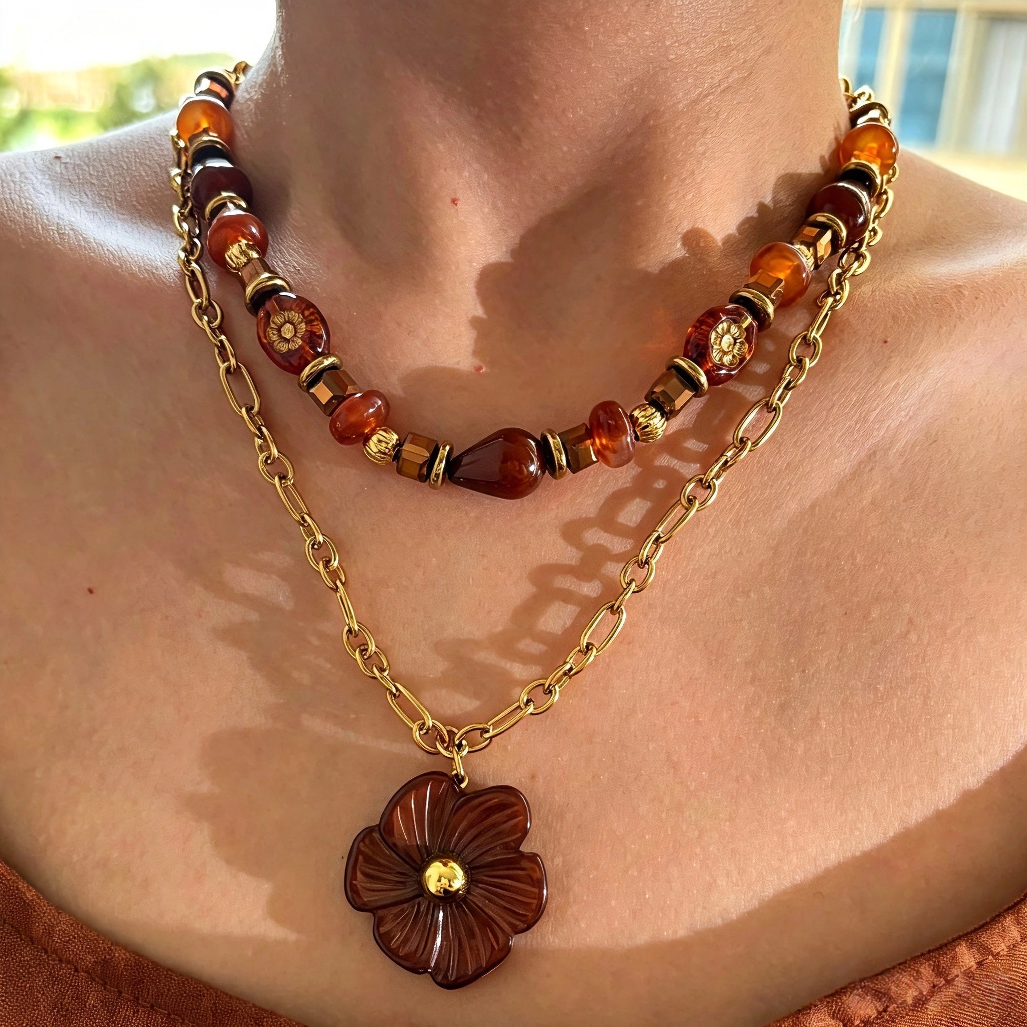 This vintage‑inspired Meidelat layered necklace features warm amber‑toned beads paired with polished gold‑toned metal chains. A carved rich brown flower pendant hangs on the lower paperclip chain, while the upper strand mixes varied-shaped resin beads for textured depth. Perfect for creating cozy boho‑chic layered neck stacking looks.