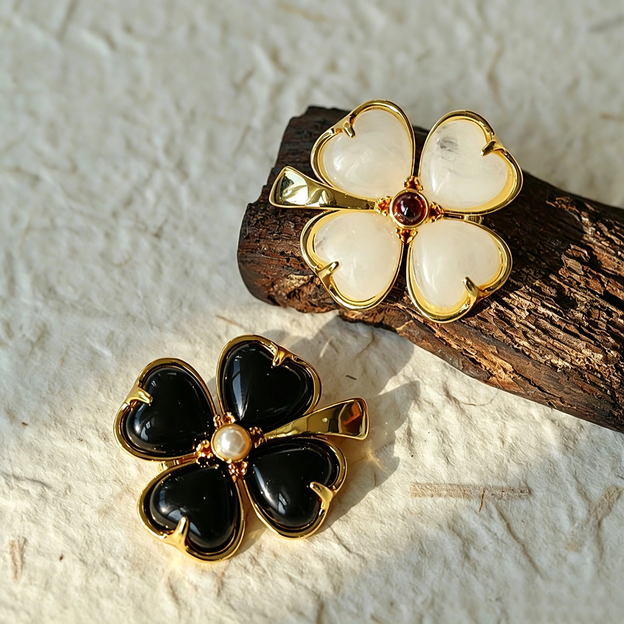 These four-leaf clover brooches come in two elegant versions: one with glossy black onyx petals centered by a delicate pearl, and the other with milky white crystal petals accented by a deep red gemstone at its core. Both are framed in polished gold-toned metal, exuding a classic, vintage-inspired charm.