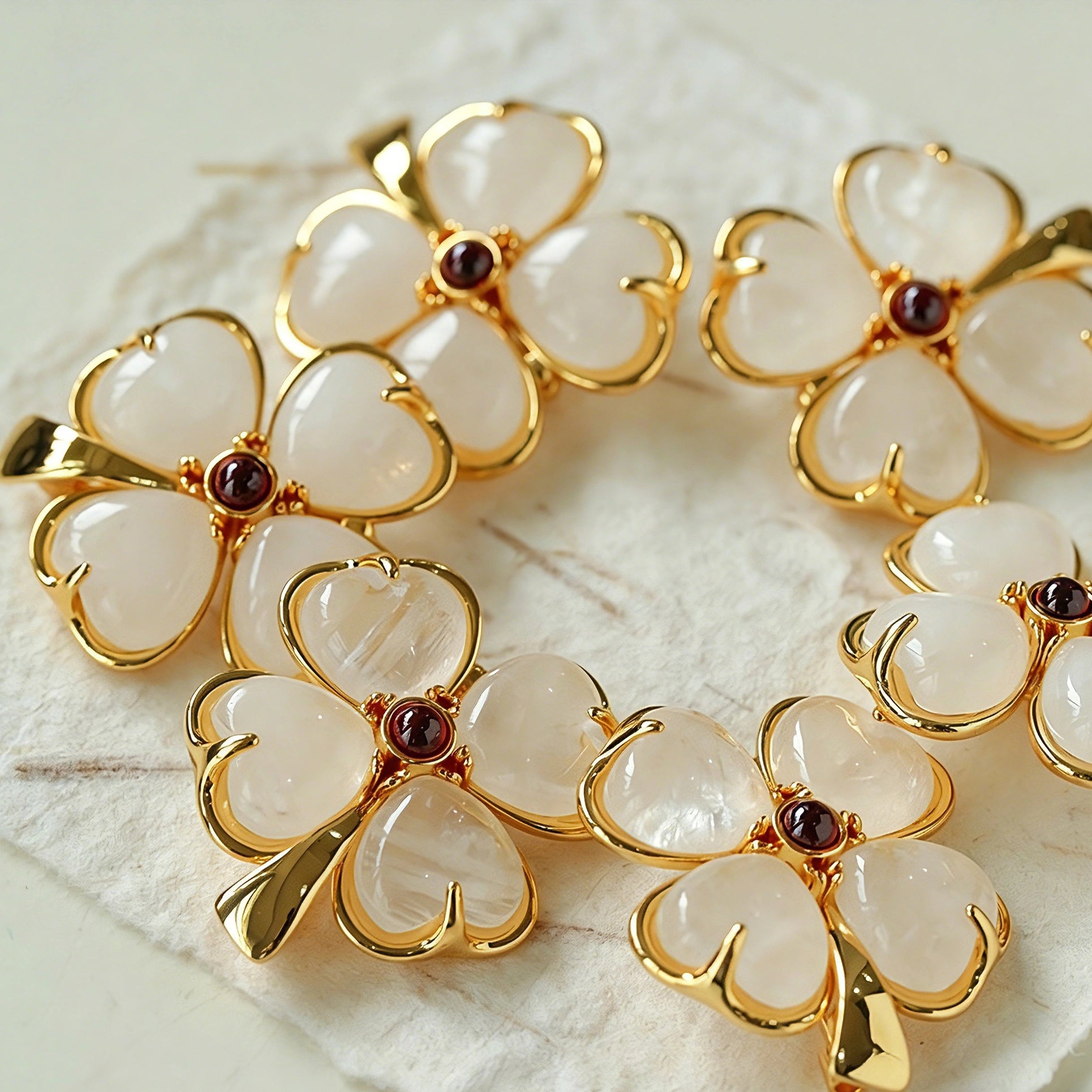 These four-leaf clover brooches come in two elegant versions: one with glossy black onyx petals centered by a delicate pearl, and the other with milky white crystal petals accented by a deep red gemstone at its core. Both are framed in polished gold-toned metal, exuding a classic, vintage-inspired charm.