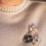 These four-leaf clover brooches come in two elegant versions: one with glossy black onyx petals centered by a delicate pearl, and the other with milky white crystal petals accented by a deep red gemstone at its core. Both are framed in polished gold-toned metal, exuding a classic, vintage-inspired charm.