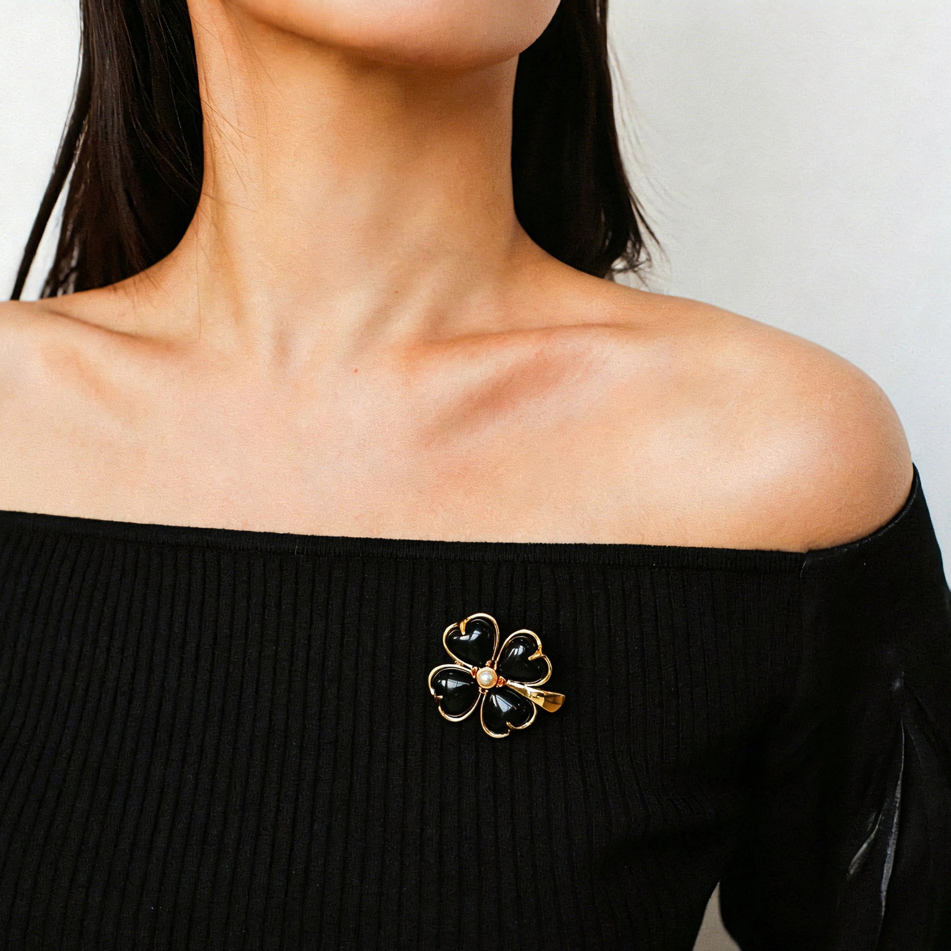 These four-leaf clover brooches come in two elegant versions: one with glossy black onyx petals centered by a delicate pearl, and the other with milky white crystal petals accented by a deep red gemstone at its core. Both are framed in polished gold-toned metal, exuding a classic, vintage-inspired charm.