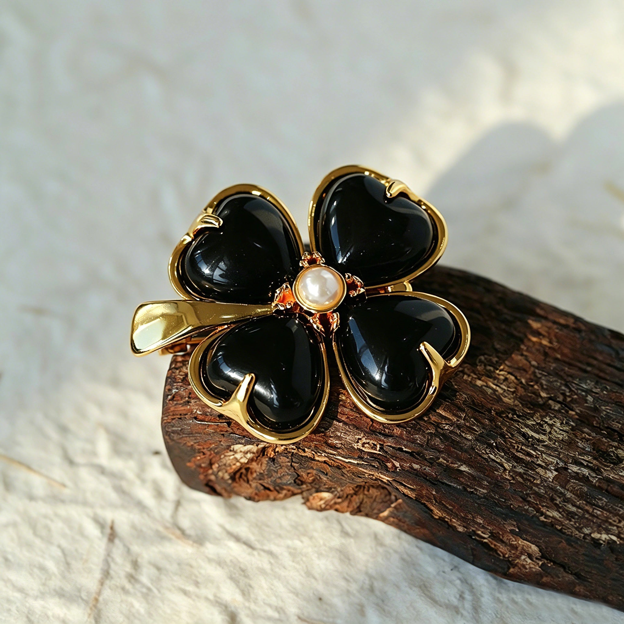 These four-leaf clover brooches come in two elegant versions: one with glossy black onyx petals centered by a delicate pearl, and the other with milky white crystal petals accented by a deep red gemstone at its core. Both are framed in polished gold-toned metal, exuding a classic, vintage-inspired charm.