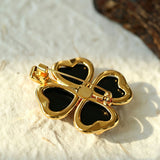 These four-leaf clover brooches come in two elegant versions: one with glossy black onyx petals centered by a delicate pearl, and the other with milky white crystal petals accented by a deep red gemstone at its core. Both are framed in polished gold-toned metal, exuding a classic, vintage-inspired charm.