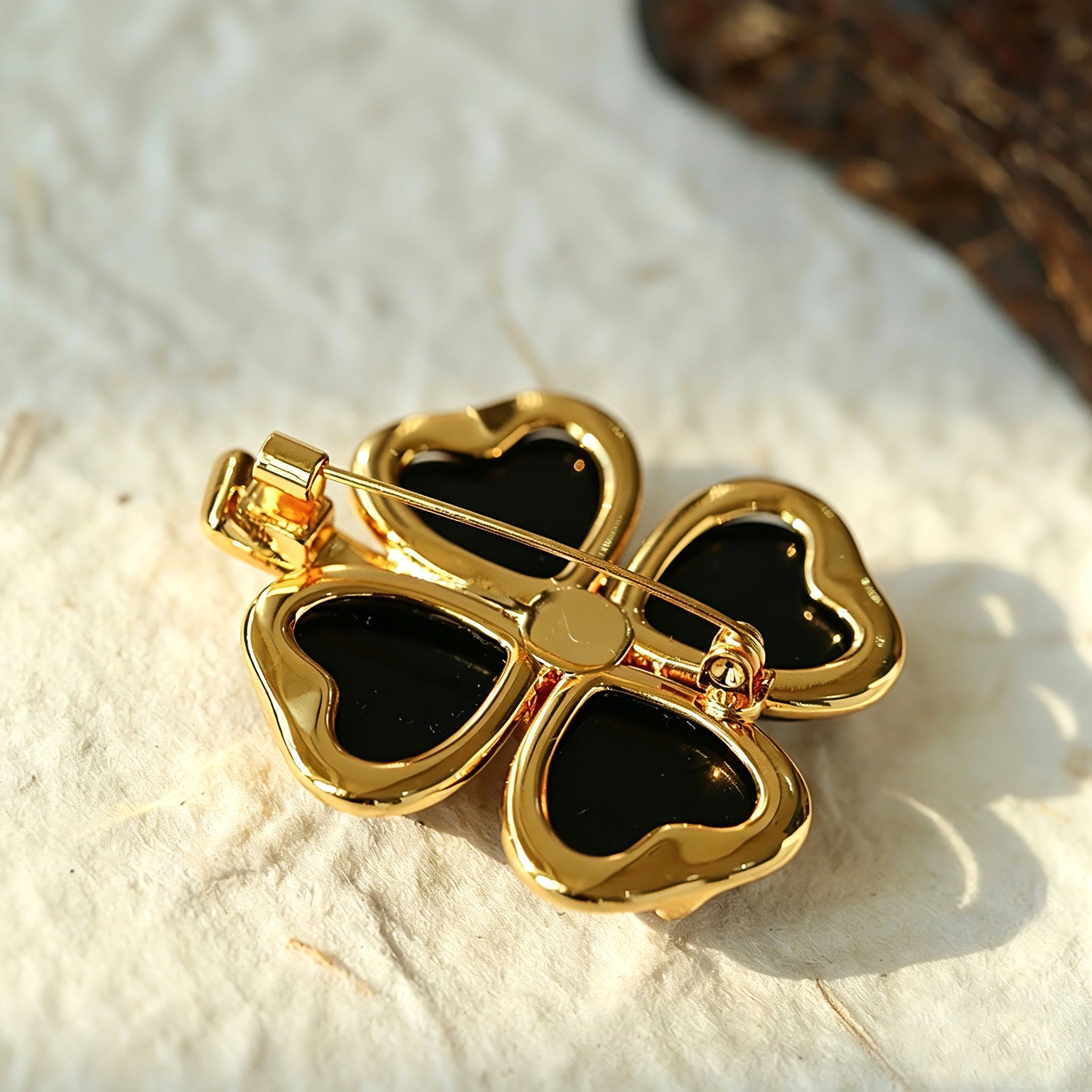 These four-leaf clover brooches come in two elegant versions: one with glossy black onyx petals centered by a delicate pearl, and the other with milky white crystal petals accented by a deep red gemstone at its core. Both are framed in polished gold-toned metal, exuding a classic, vintage-inspired charm.
