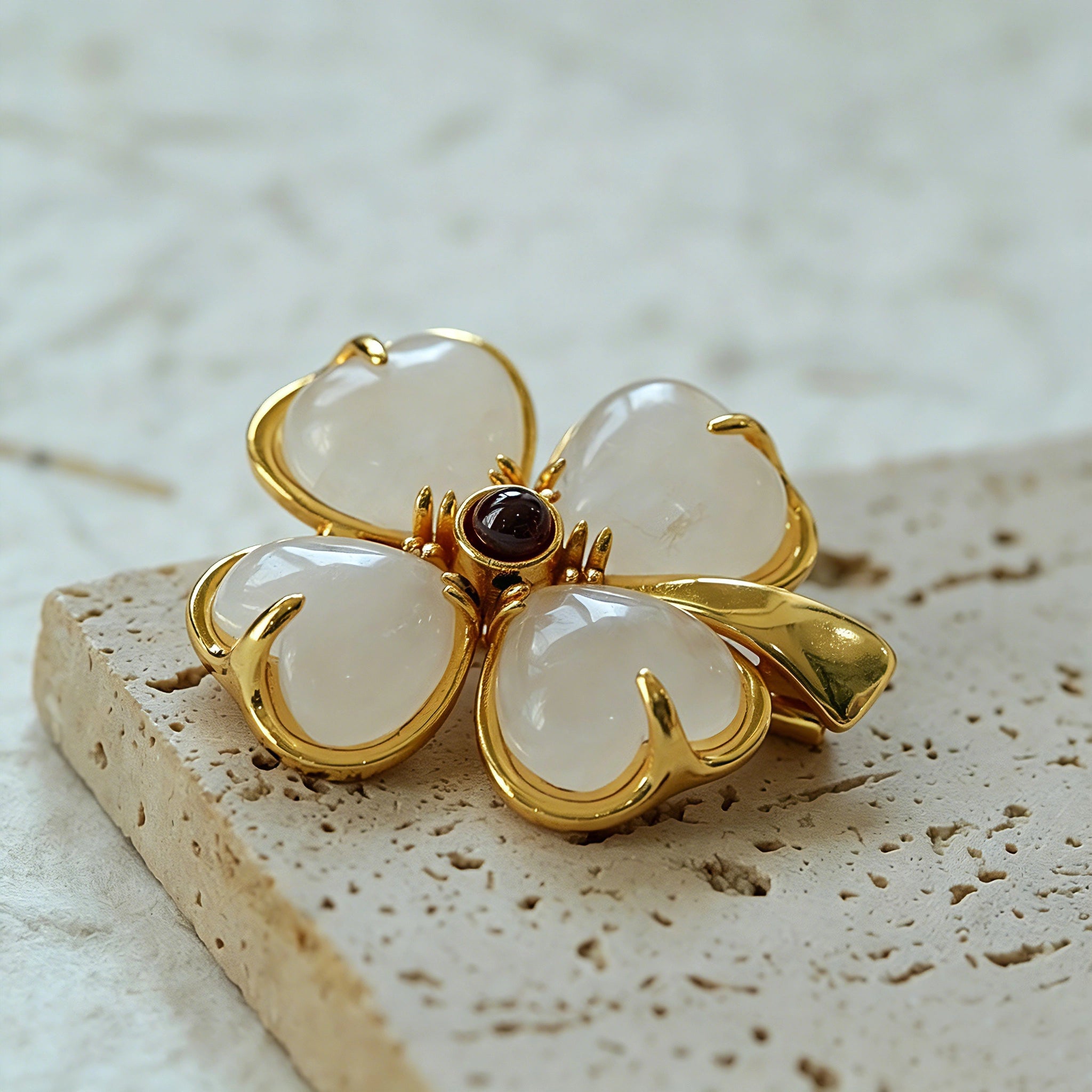 These four-leaf clover brooches come in two elegant versions: one with glossy black onyx petals centered by a delicate pearl, and the other with milky white crystal petals accented by a deep red gemstone at its core. Both are framed in polished gold-toned metal, exuding a classic, vintage-inspired charm.