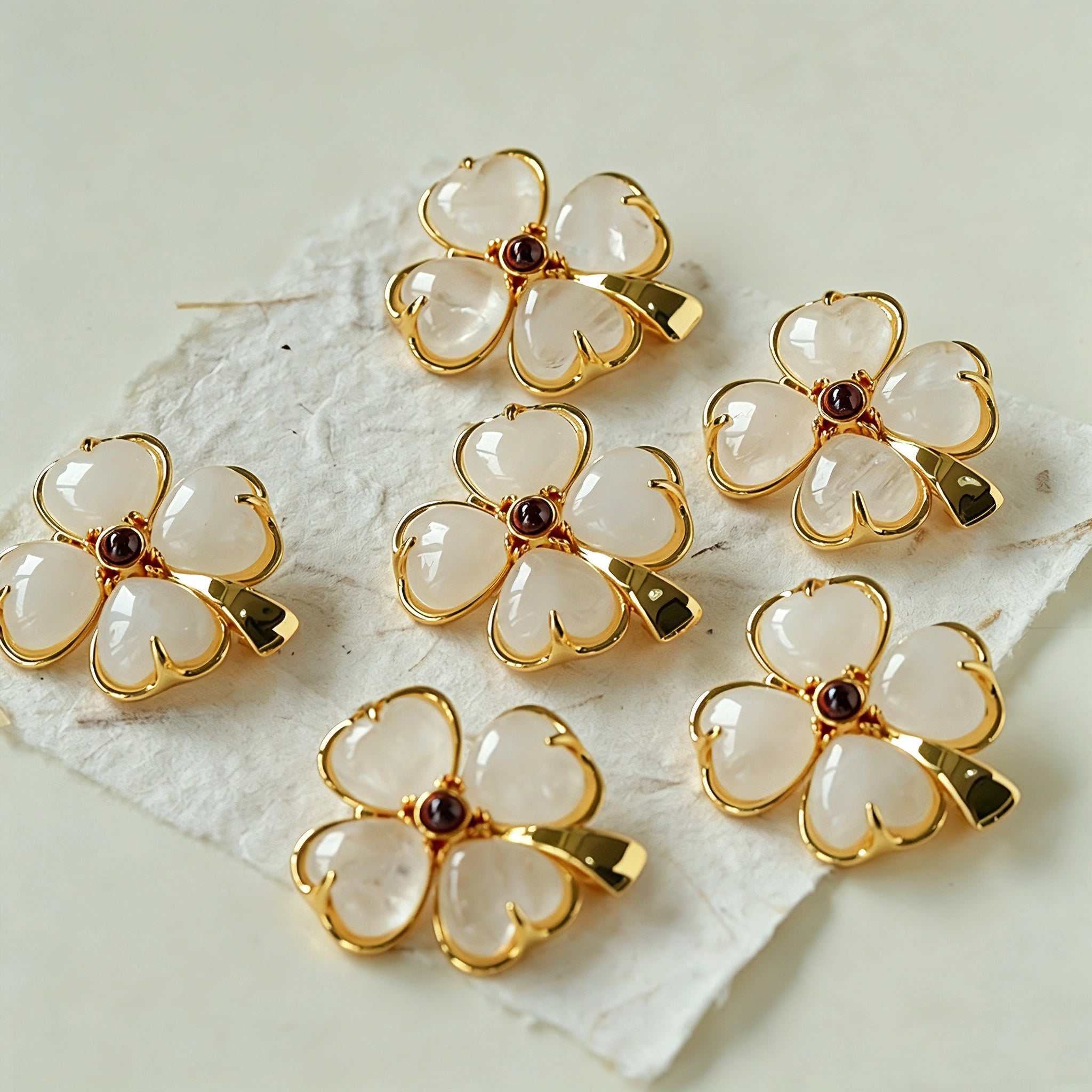 These four-leaf clover brooches come in two elegant versions: one with glossy black onyx petals centered by a delicate pearl, and the other with milky white crystal petals accented by a deep red gemstone at its core. Both are framed in polished gold-toned metal, exuding a classic, vintage-inspired charm.